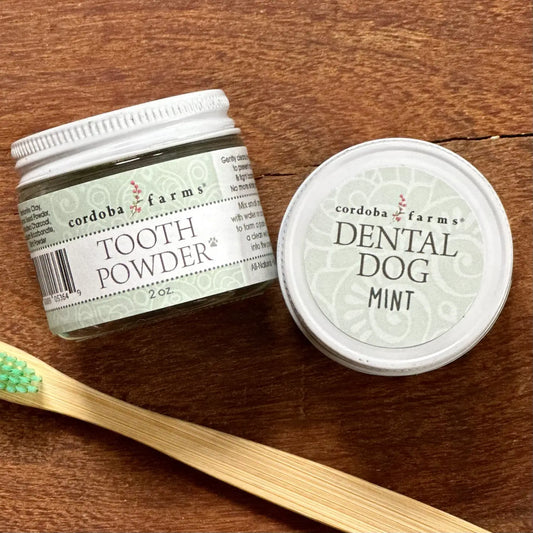 Two Cordoba Farms tooth powder jars and a bamboo dog toothbrush with green bristles