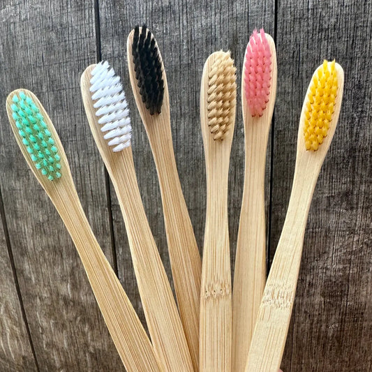 Six different colored bambook toothbrushes with a wooden background
