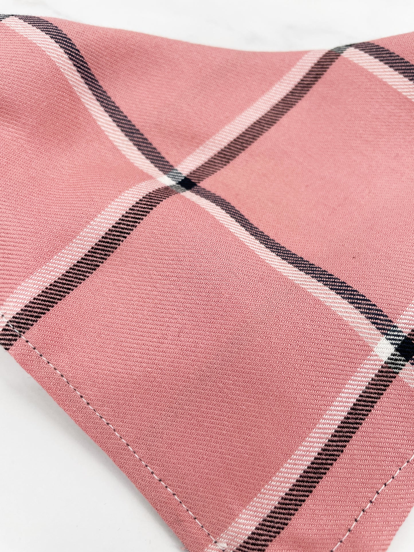 close up of the soft cotton fabric of the light pink dog bandana with white and black plaid stripes
