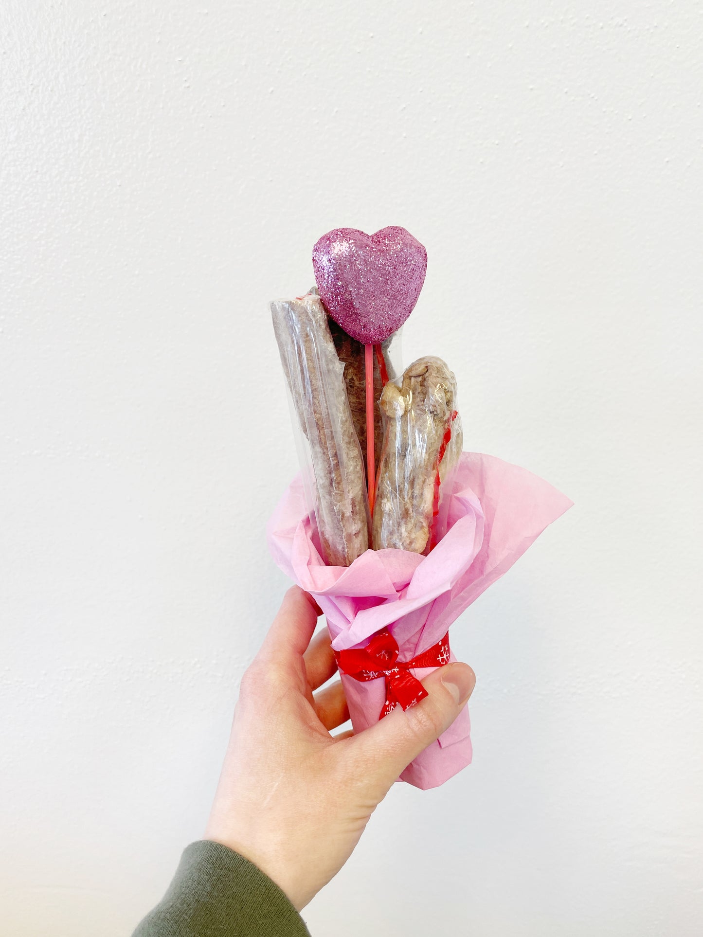 Hand holding a bouquet of bones with a decorative pink heart in the middle
